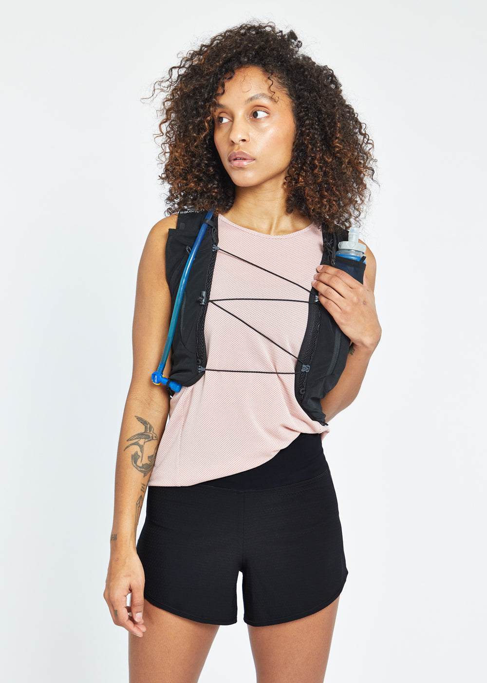 Woman wearing High Rise Roga 4" Running Shorts in black, paired with Flyout Trail Tank and hydration vest